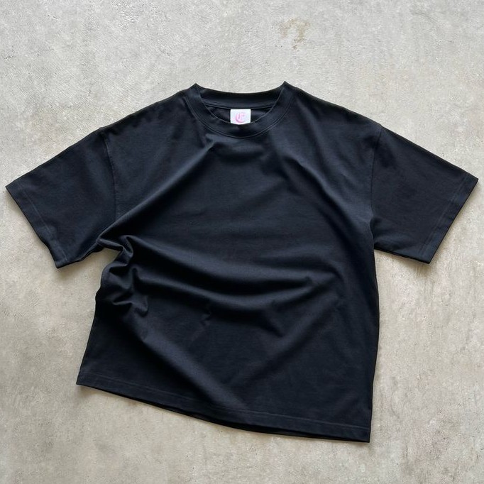Plain black T-shirt laid flat on a light concrete background
