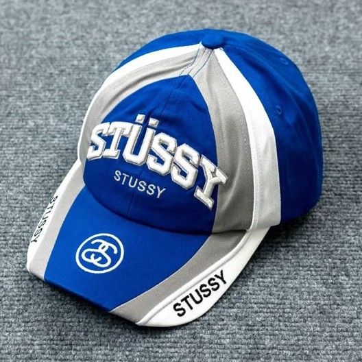 Blue cap with white and grey panels and embroidered lettering on grey fabric