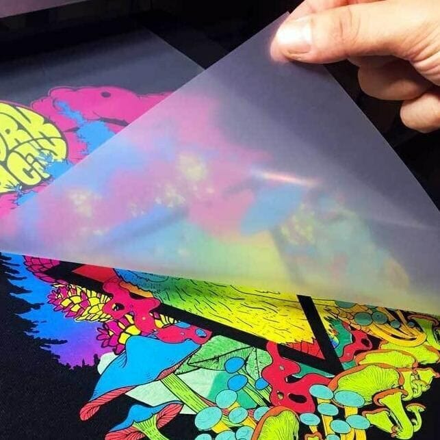 Transfer film being peeled from a colourful DTF print on black fabric