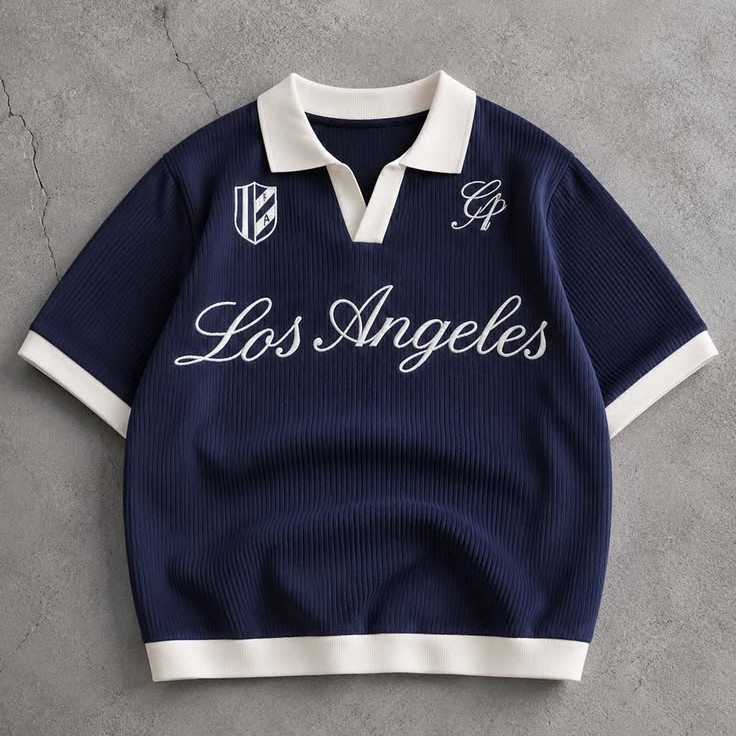 Navy polo shirt with cream trim and Los Angeles lettering laid flat on concrete