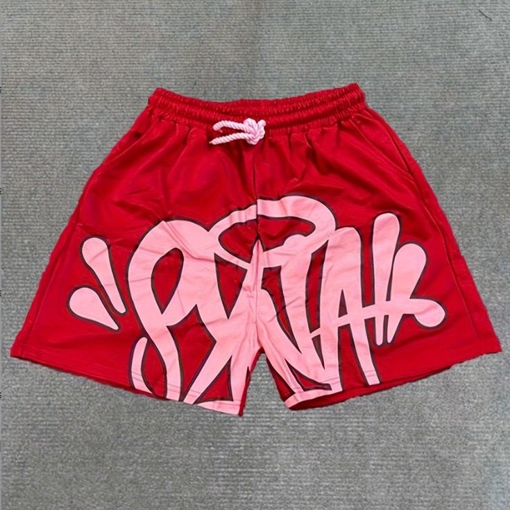 Red shorts with pink lettering and a white drawstring laid flat on grey fabric