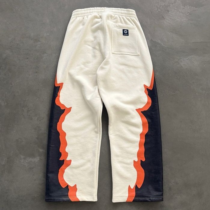 Cream track pants with orange and black side panels laid flat on concrete