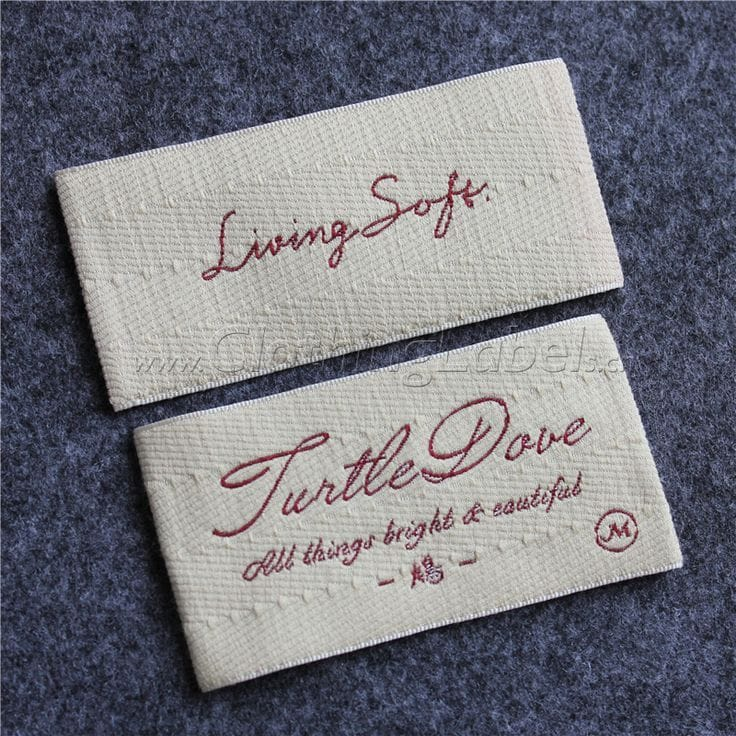 Two cream woven clothing labels on grey fabric